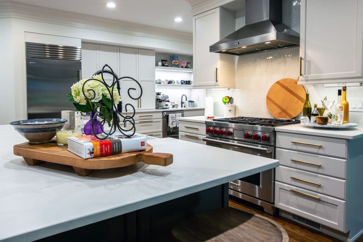 Kitchen detail with a Wolf range under a stainless hood, geometric tile backsplash, brass hardware and a quartz waterfall island