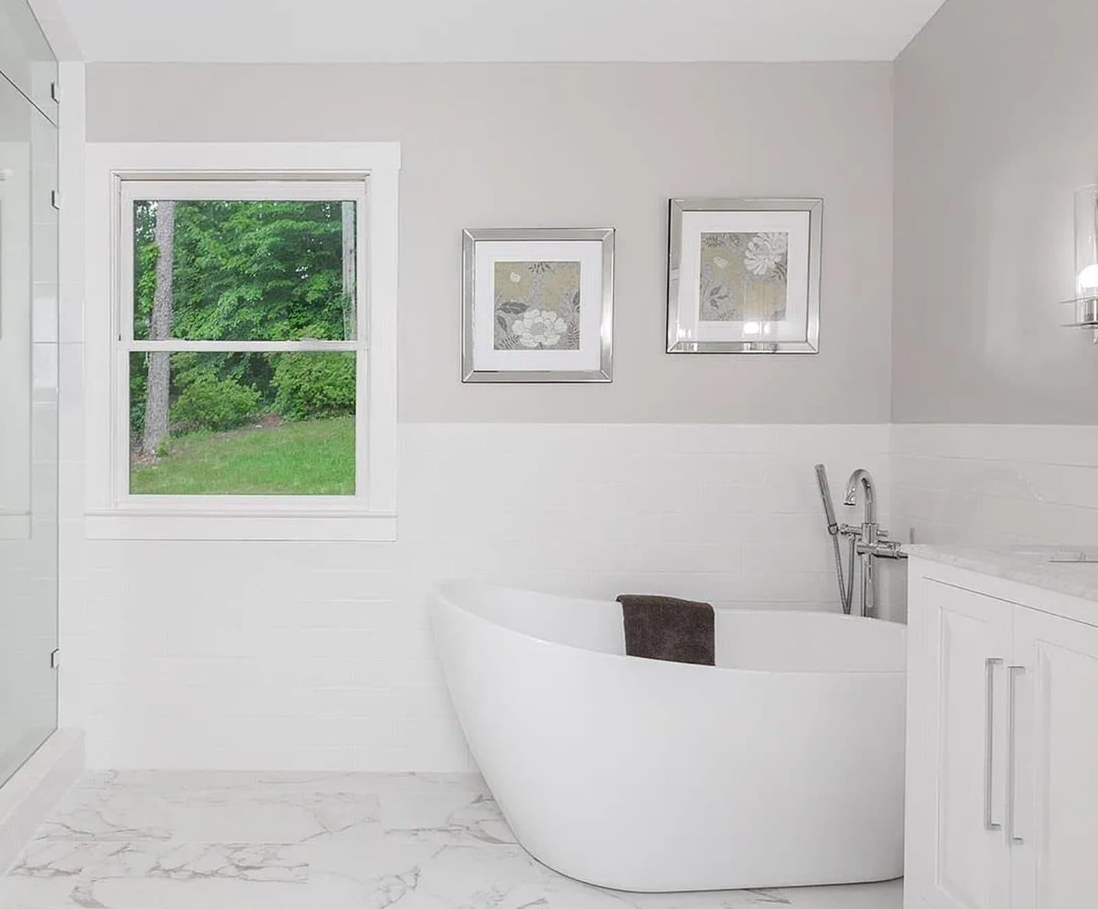 Primary bathroom with a freestanding soaking tub, floor-mounted filler, subway-tiled wainscot and marble-look porcelain floor